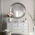 Okragłe lustro Aurora Silver ze srebrną mozaiką w stylu glamour nad białą komodą w salonie. GieraDesign