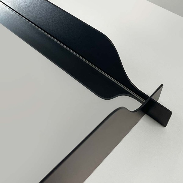 Zbliżenie na czarną, metalową rozszerzającą się środkiem ramę lustra Monda Flo prostokątne autorstwa Nikodema Szpunara.