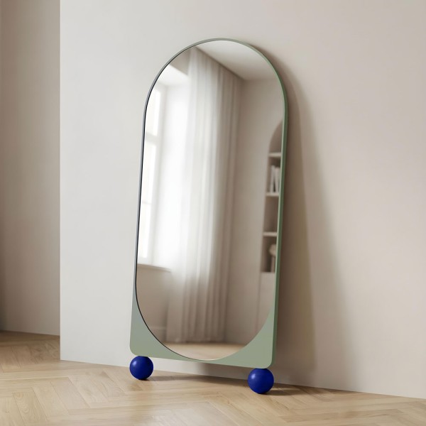 Lustro stojące na kulach noom, w kolorze miętowym, o parte o ścianę. GieraDesign