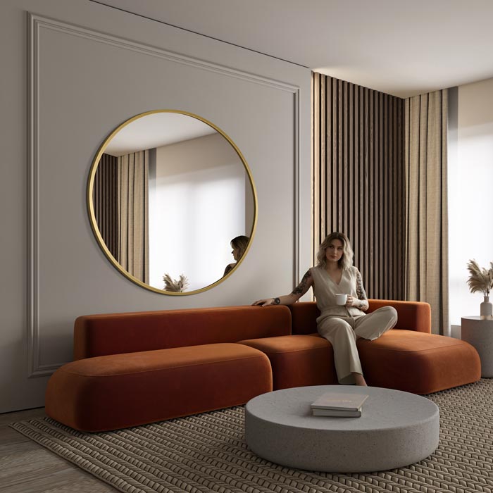 Duże lustro w złotej ramie Scandi w nowoczesnym salonie, zawieszone nad kanapą na ścianie prostopadłej do okna odbija naturalne światło i rozświetla wnętrze