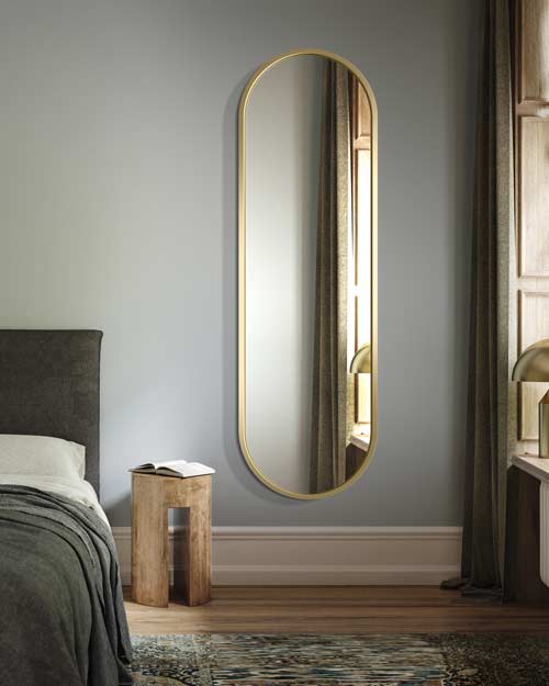 Podłużne lustro owalne Ambient ze złotą ramą w sypialni  
