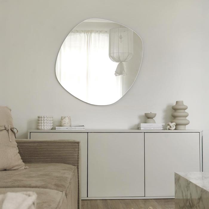 Nieregularne  lustro Roco Wide zawieszone nad komodą naprzeciw oknaw nowoczesnym salonie